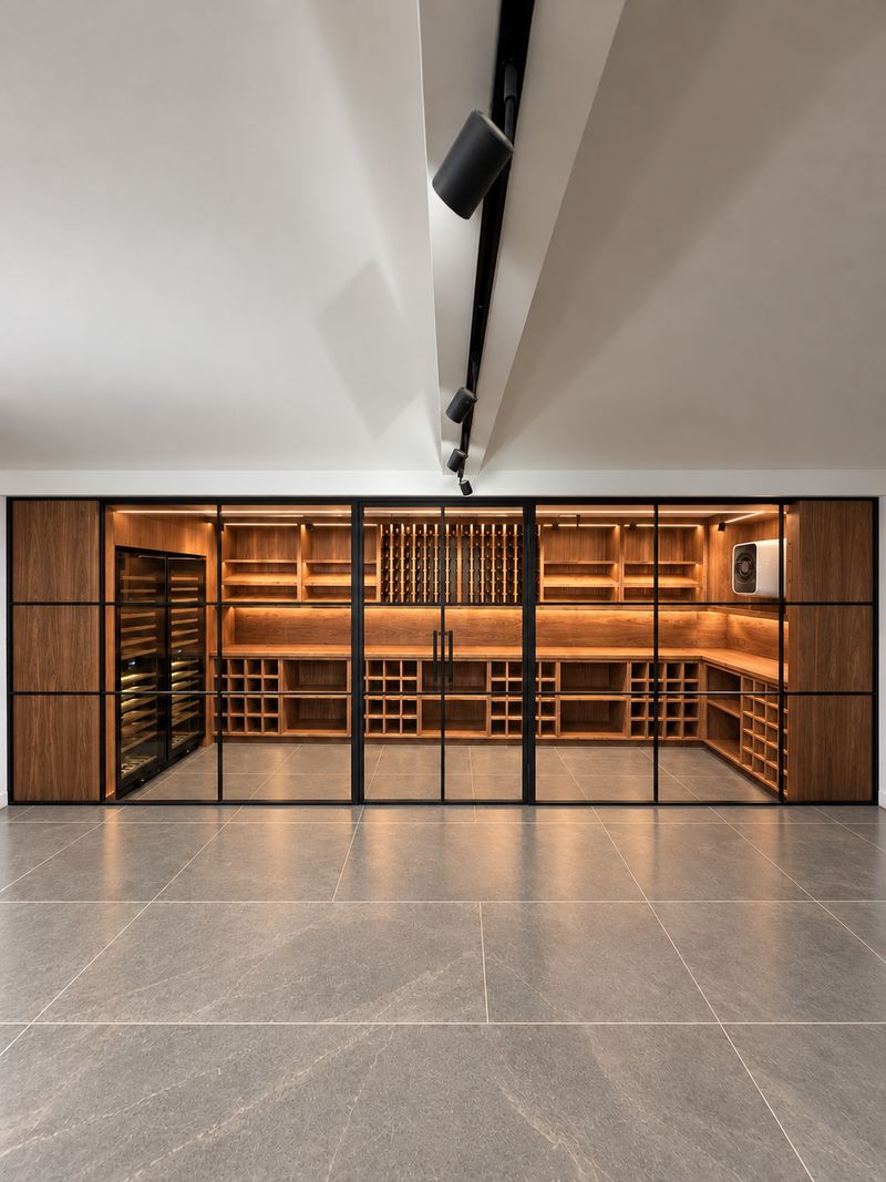 Walnut wine cellar joinery behind steel-framed glass doors